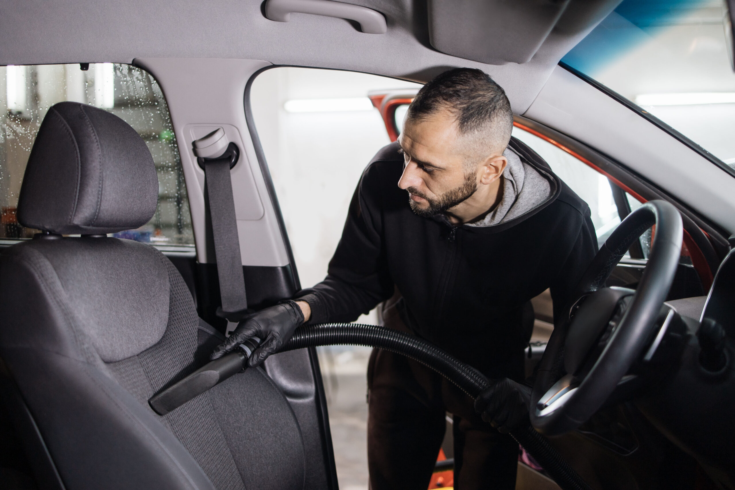 professional young male worker using vacuum cleaner for dirty car interior.